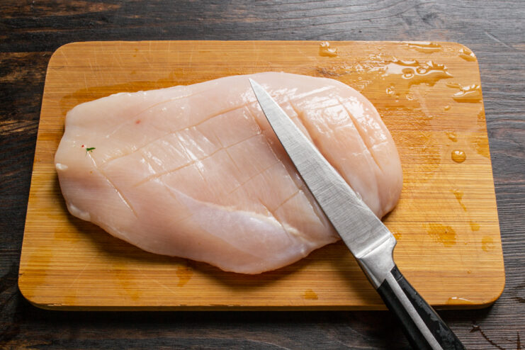 Prepping the chicken Scored raw chicken breast lying on a wooden cutting board