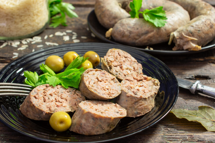 Sliced homemade chicken liver and rice sausage on a plate with olives and parsley.