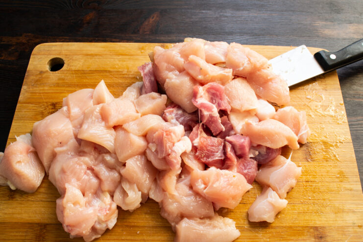 Prepping the meat for meatballs Diced chicken fillet and pork pieces on a wooden cutting board