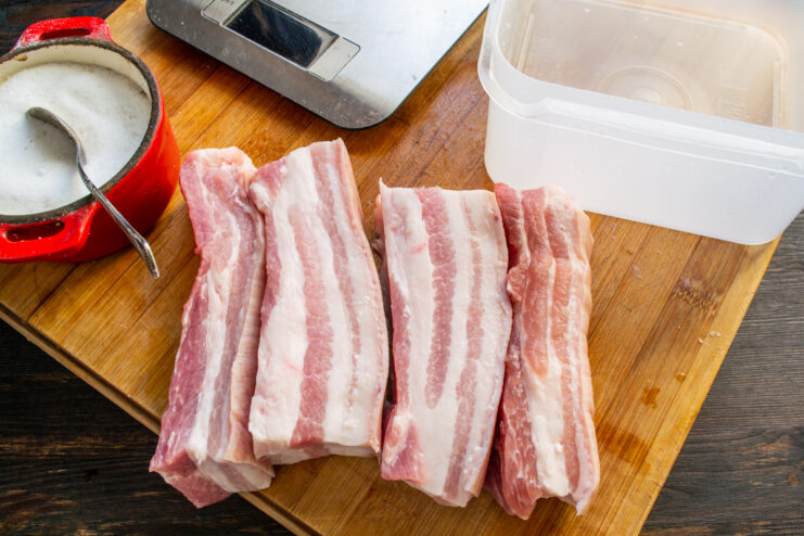 Sliced pieces of raw pork belly arranged on a wooden cutting board