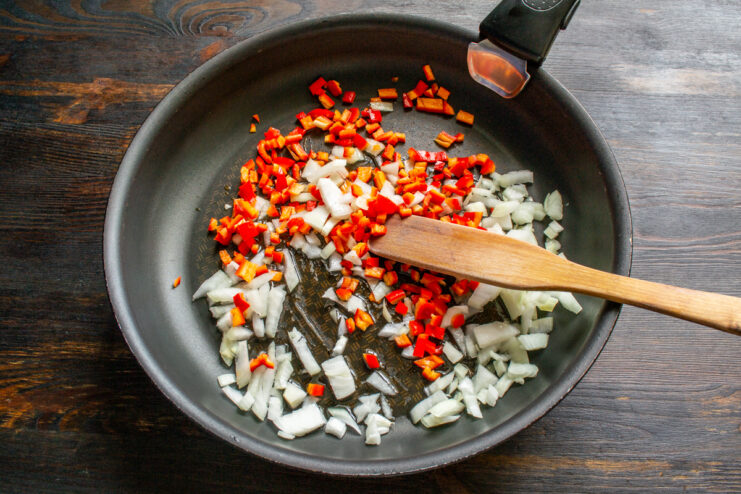 Sautéing The Vegetables Diced onion and red bell pepper cooking in a skillet