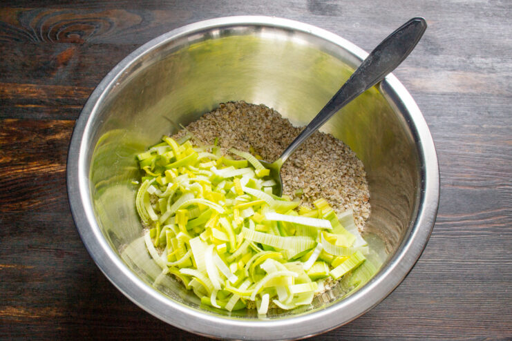 Chopped leeks added to a bowl of ground oats