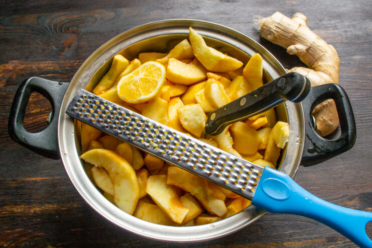 Adding fresh lemon zest and ginger Grating fresh lemon zest directly into the pot with chopped apples.