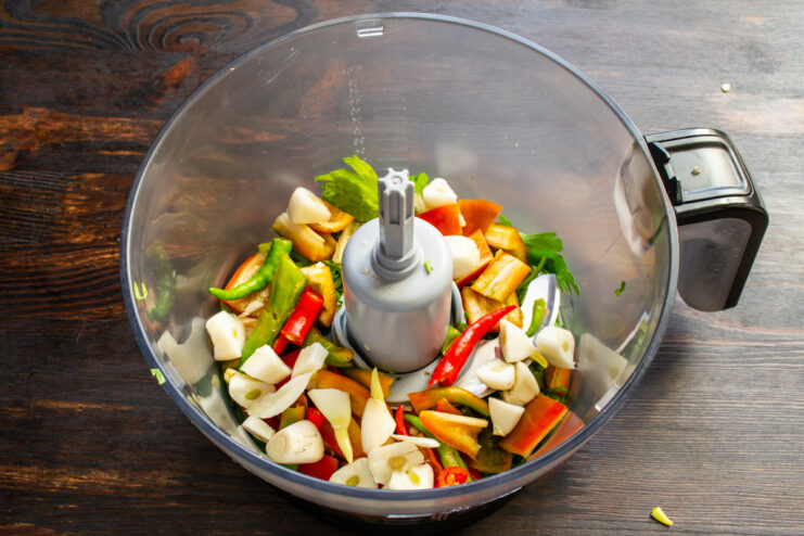 Mixing fresh garlic into the adjika Peeled and chopped garlic cloves in the blender bowl with peppers and greens.