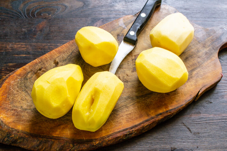 Peeled raw potatoes resting on a wooden cutting board