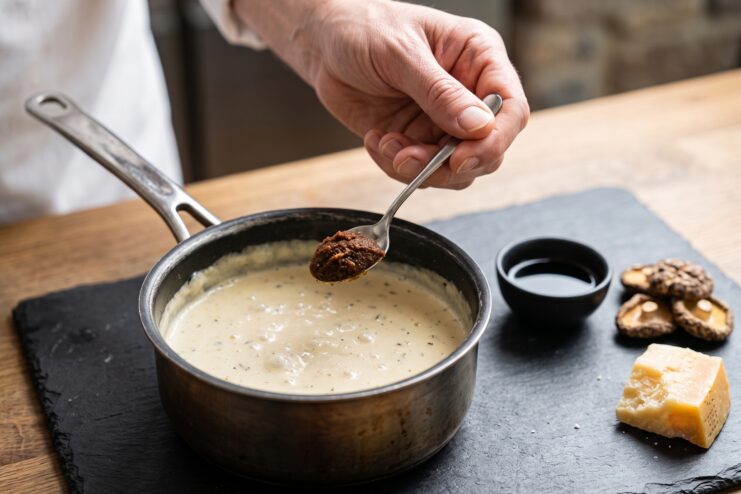 Stirring miso paste into cream sauce Chef whisking a spoonful of miso paste into a saucepan filled with a white cream sauce.