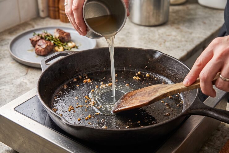 Deglazing a cast iron skillet Chef pouring broth into a hot cast iron skillet filled with browned meat bits to create a pan sauce.