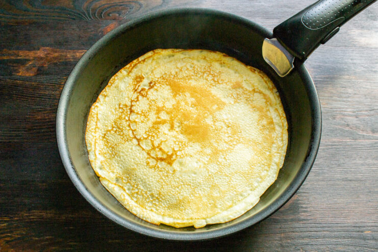 Cooking The Crepes Flipping a thin golden crepe cooking in a hot round skillet