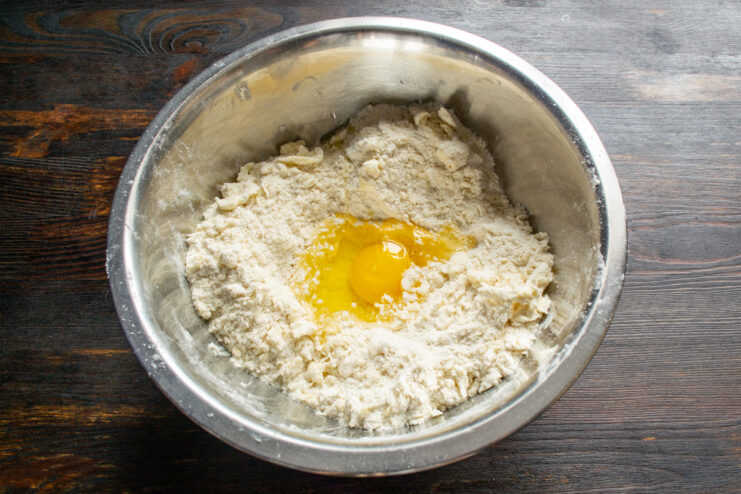 Cracking an egg and pouring milk into the crumbly flour mixture