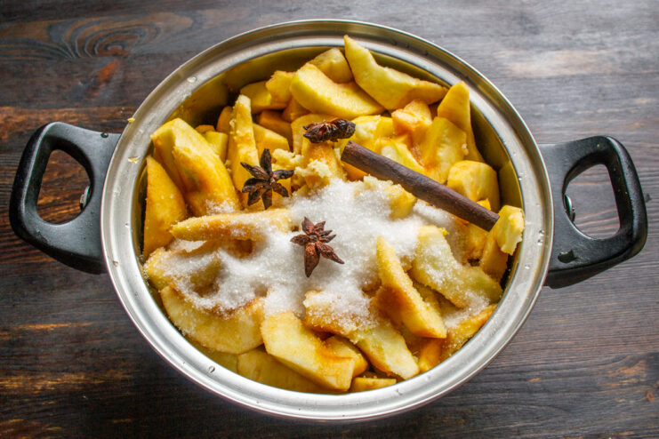 Adding cinnamon and star anise Sugar, a cinnamon stick, and star anise pods on top of chopped apples in a pot.