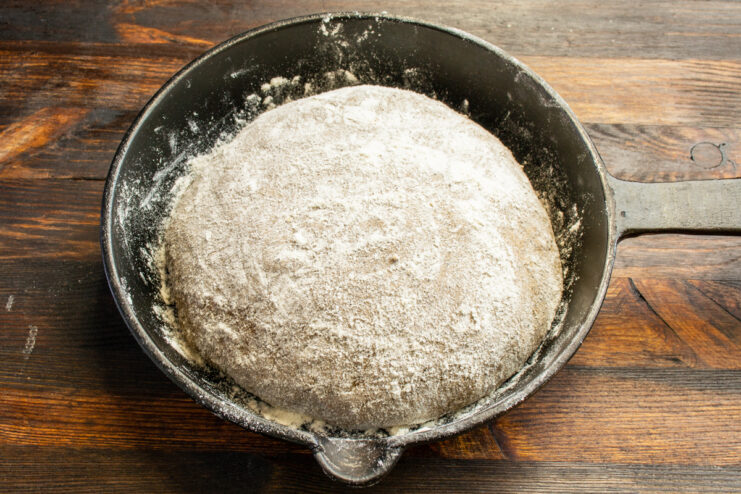Shaped dough boule resting in a floured cast-iron skillet