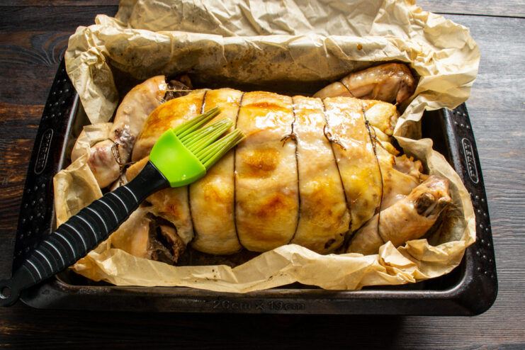 Basting a roasting stuffed chicken with pan juices using a brush.