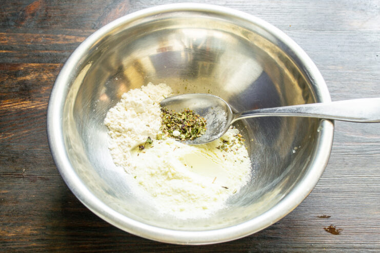 Mixing milk powder, flour, and dried herbs in a bowl