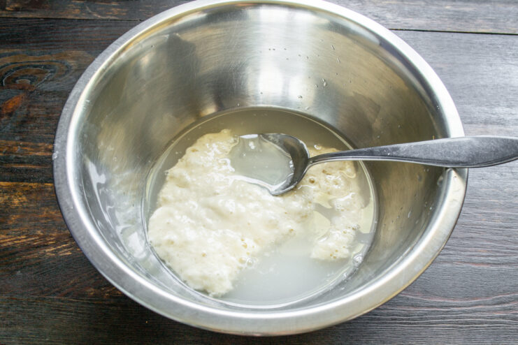Mixing sourdough starter with water in a metal bowl