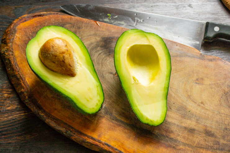 Preparing the Avocado Ripe avocado halved with pit removed on a wooden cutting board