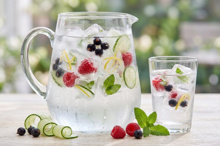 Refreshing water with beautiful berry and vegetable ice Glass pitcher and cup of water with ice featuring frozen berries, cucumber, and mint leaves.