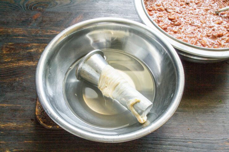 Preparing The Casing Pork casing threaded onto a sausage stuffer attachment over a bowl of water.