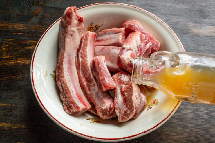 Marinating in Vinegar Pouring apple cider vinegar over raw pork ribs in a mixing bowl
