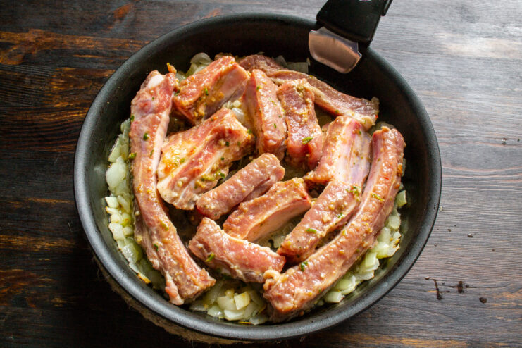 Searing the Meat Pork ribs searing in a large skillet with sautéed onions