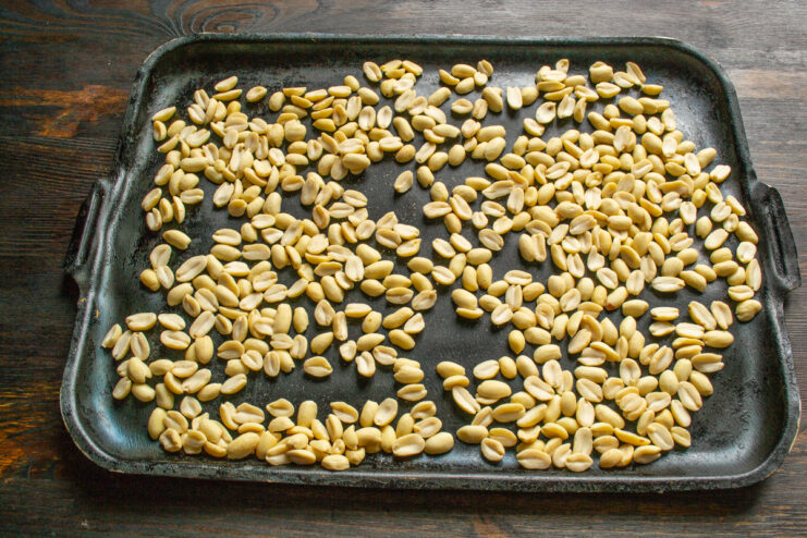 Raw peeled peanuts spread evenly on a metal baking sheet.