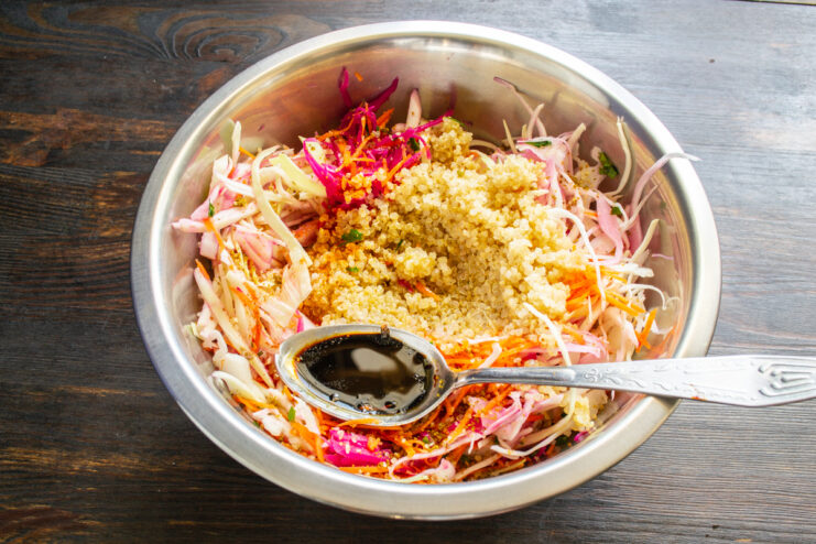 Dark soy sauce in a measuring spoon held over a bowl of fresh salad.