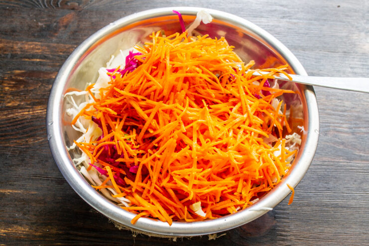 Finely grated carrot placed on top of shredded cabbage in a bowl.