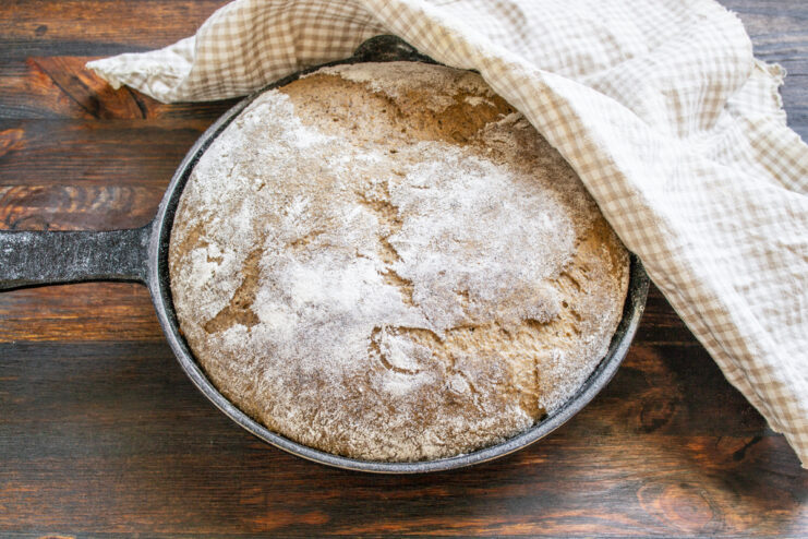 Bread dough in a skillet covered with a kitchen towel