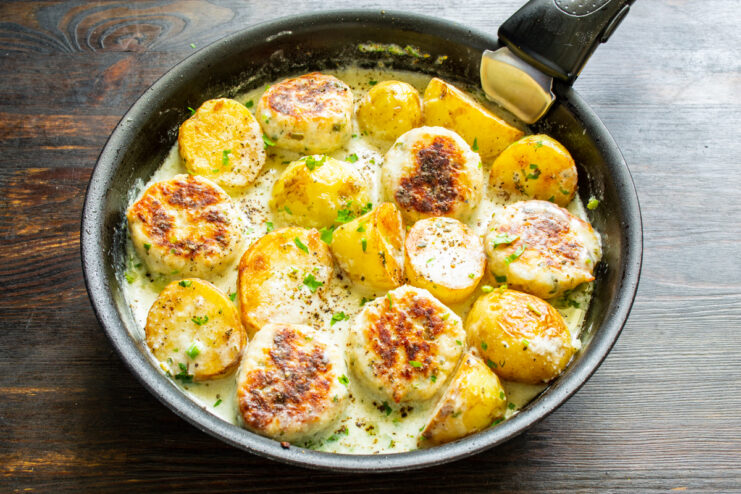 Simmering potatoes and meatballs covered in a skillet