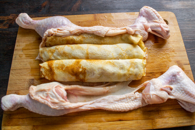 Placing the first layer of stuffed crepe tubes onto the chicken skin.
