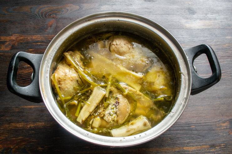 Making the chicken broth Chicken boiling in a pot with fresh herbs and root vegetables