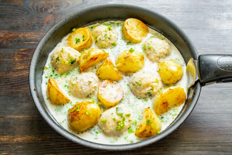 Pouring creamy sauce over potatoes and meatballs in a skillet