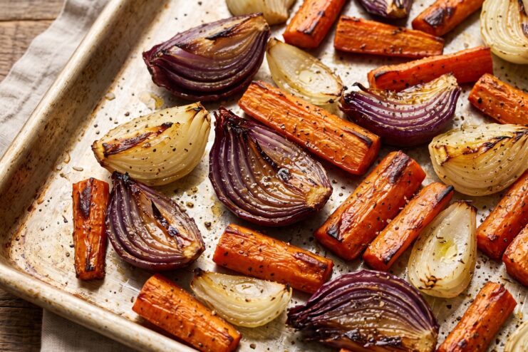 Caramelizing vegetables on a baking sheet Roasted, golden-brown caramelized chunks of carrots and red onions scattered on a baking sheet.