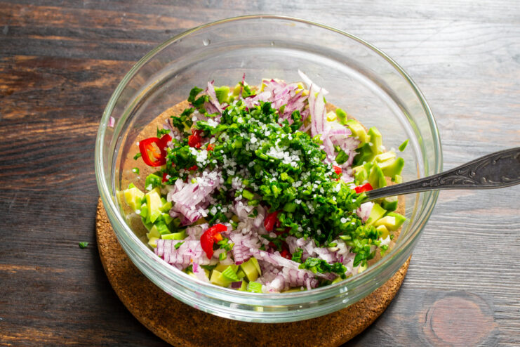 Adding Herbs and Salt Chopped herbs and sea salt added to avocado and onions in a bowl