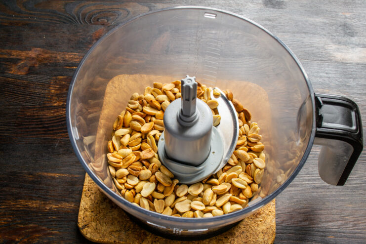 Warm roasted peanuts placed inside a food processor bowl.