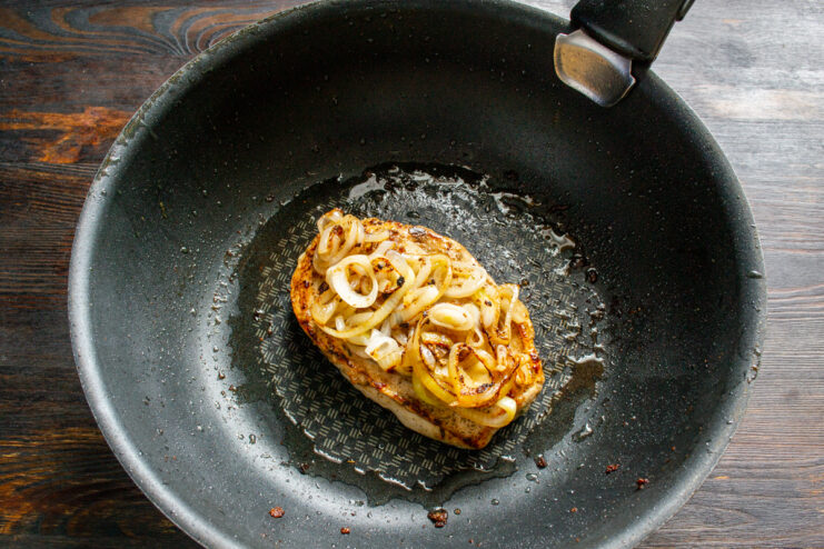 Layering onions on chicken Spatula placing fried onions on top of a seared chicken breast