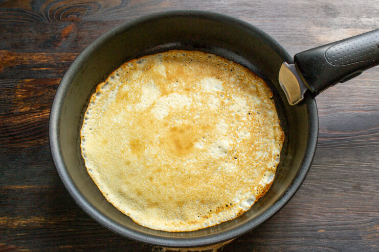 Frying a thin crepe in a hot skillet.