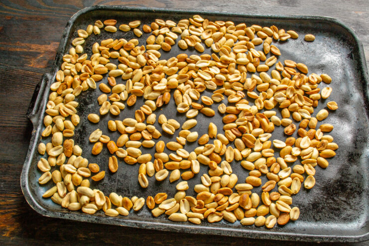 Golden roasted peanuts on a dark baking sheet.